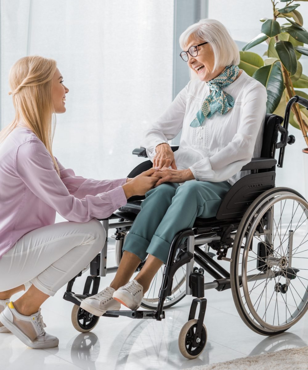 young woman speaking with senior woman in wheelchair at nursing home